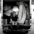 Person sitting on the bed of the Bridging truck full of furniture.